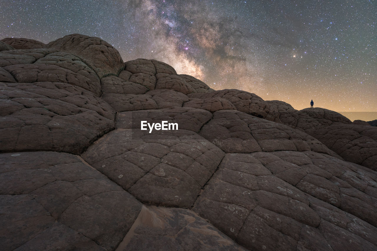 Silhouette of unrecognizable explorer standing on scenery of rocky formations in highlands under milky way starry sky in vermillion cliffs national monument, arizona in usa