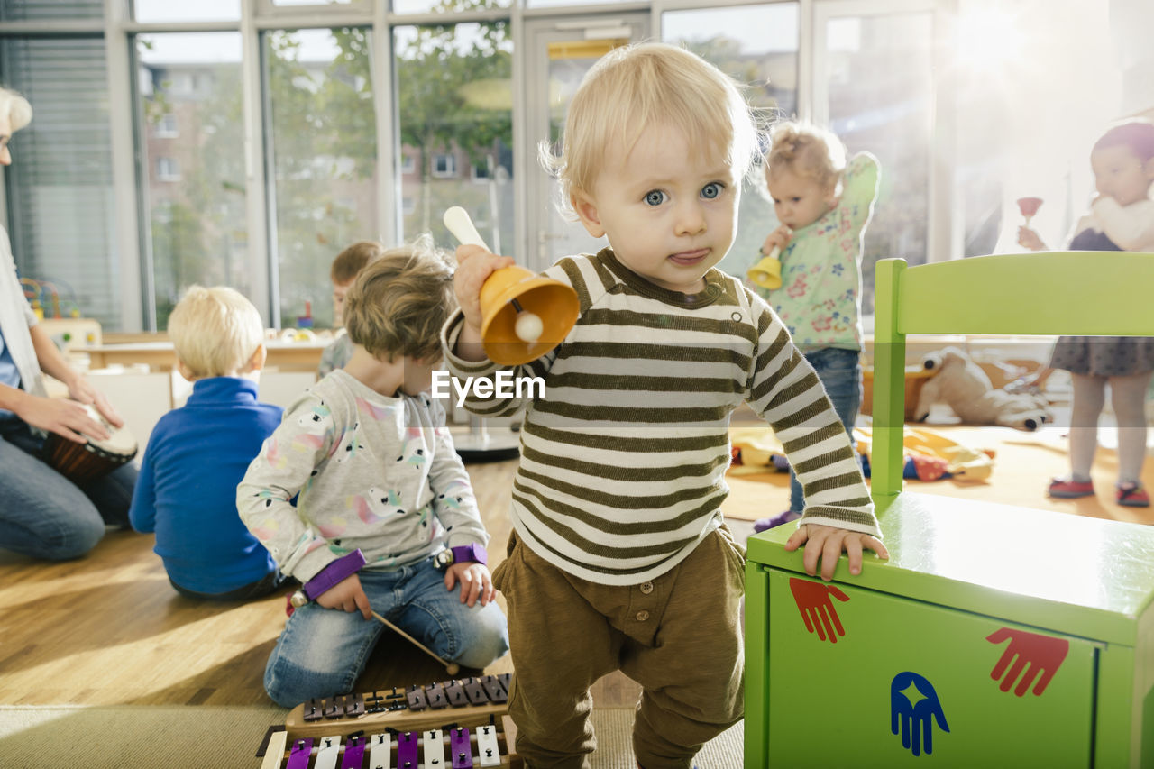 Toddler ringing a bell in music room of a kindergarten