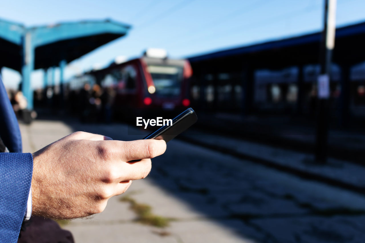 Close-up of businessman texting on mobile phone at train station.