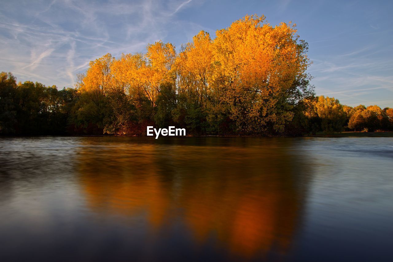 Scenic view of lake by trees against orange sky