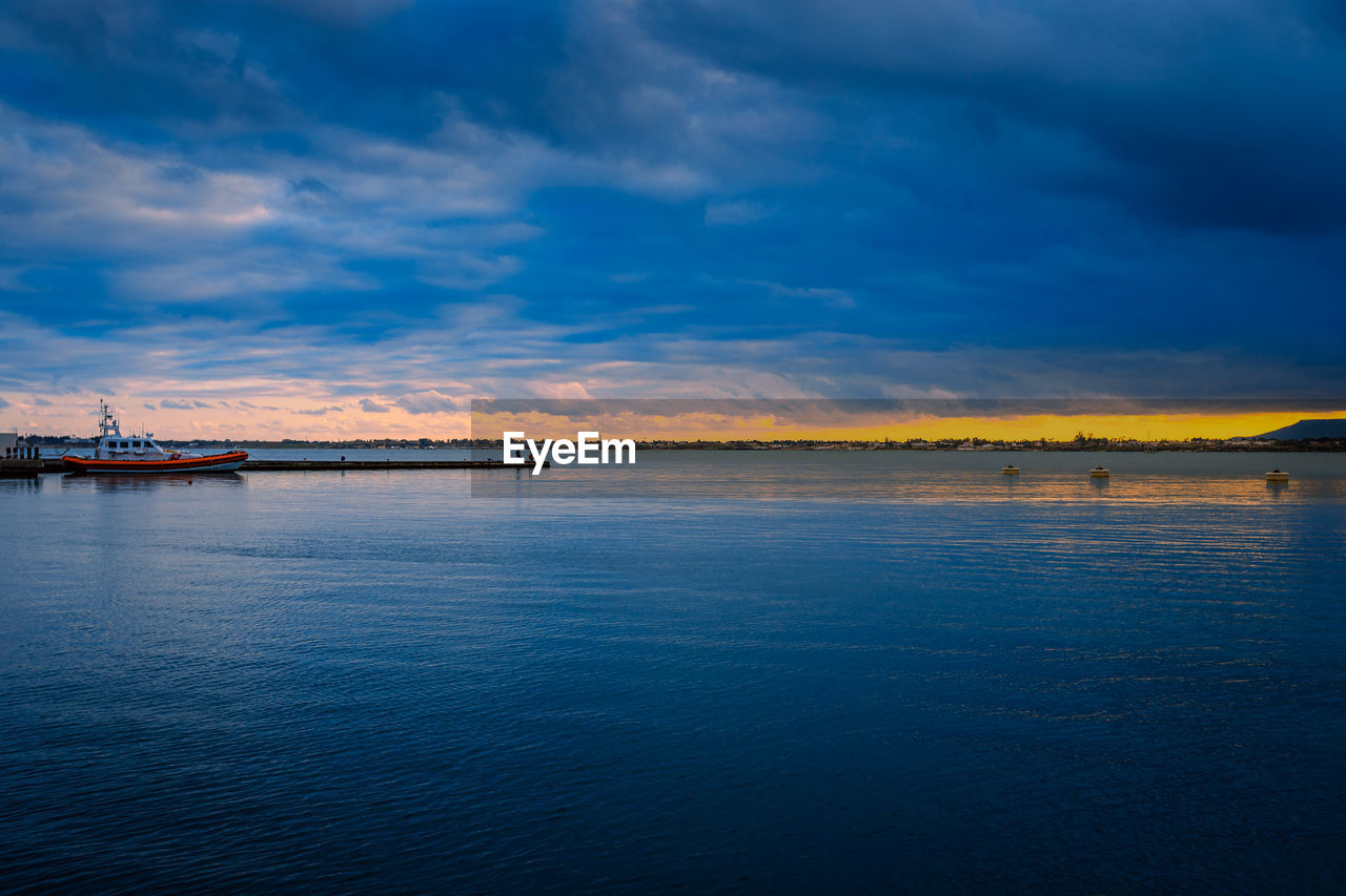 Sunset on the sea with cloudy sky and small harbor with dinghy and people