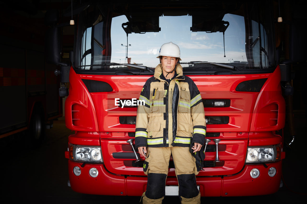 Portrait of female firefighter standing in front of fire engine at fire station