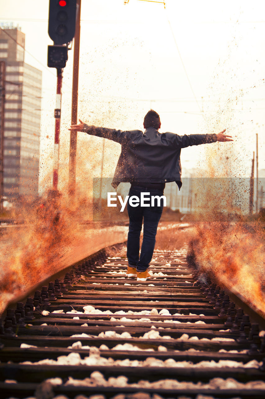 Rear view of man throwing sand while walking on railroad track