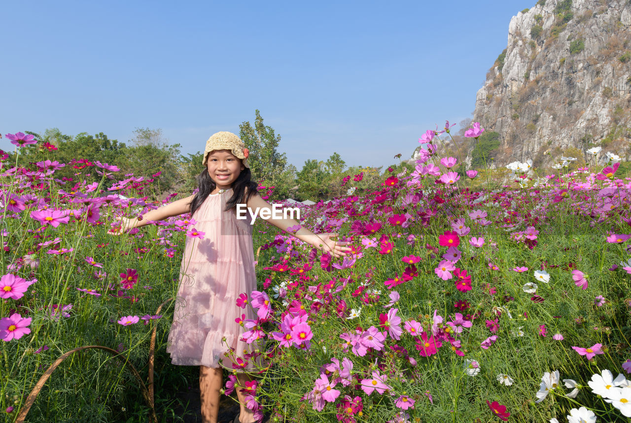 Portrait of smiling young woman standing by pink flowering plants