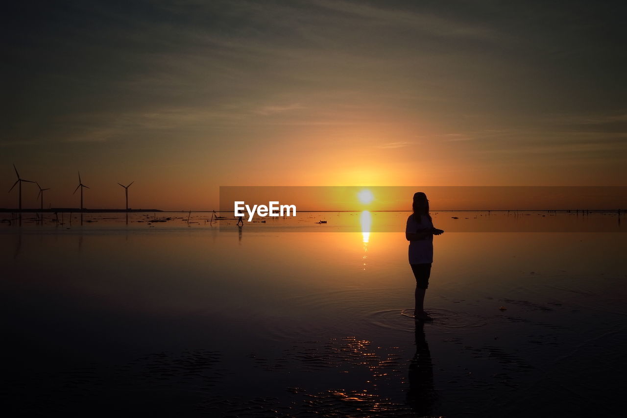 Silhouette woman standing on beach at sunset