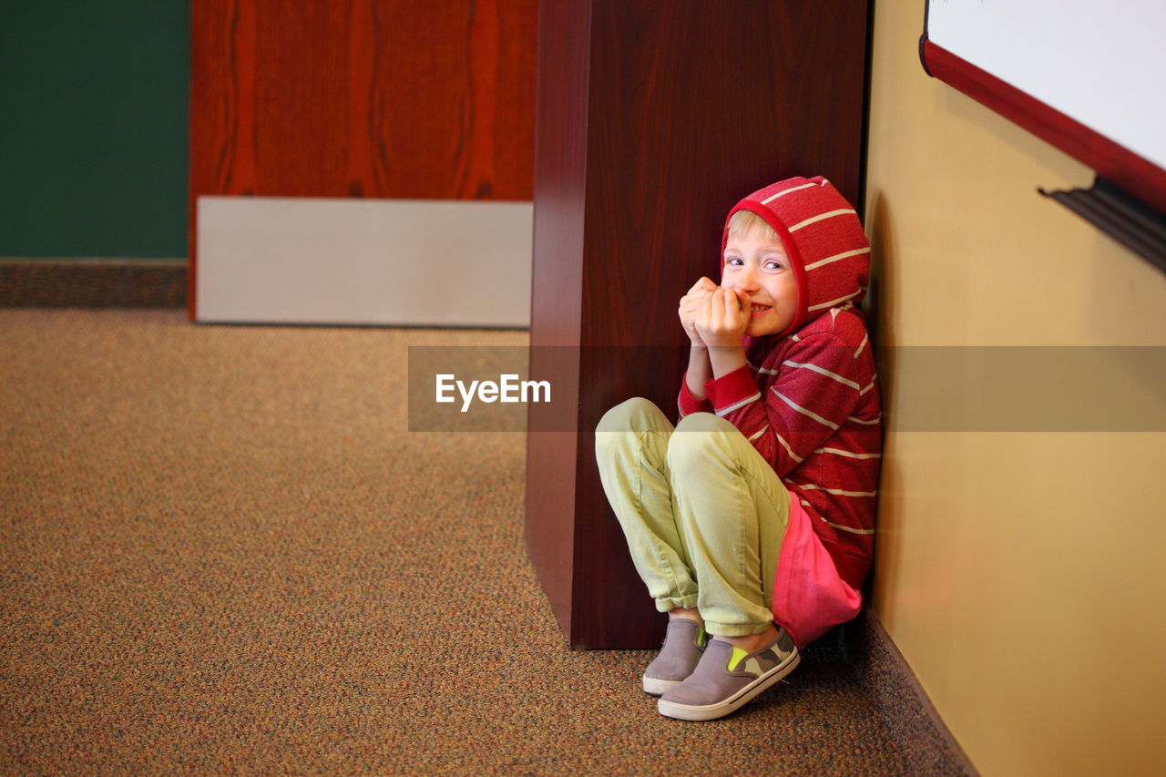 Portrait of scared child hiding by wall