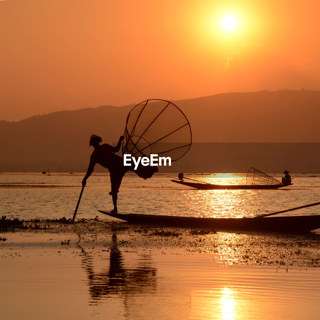 Silhouette men fishing in lake during sunset