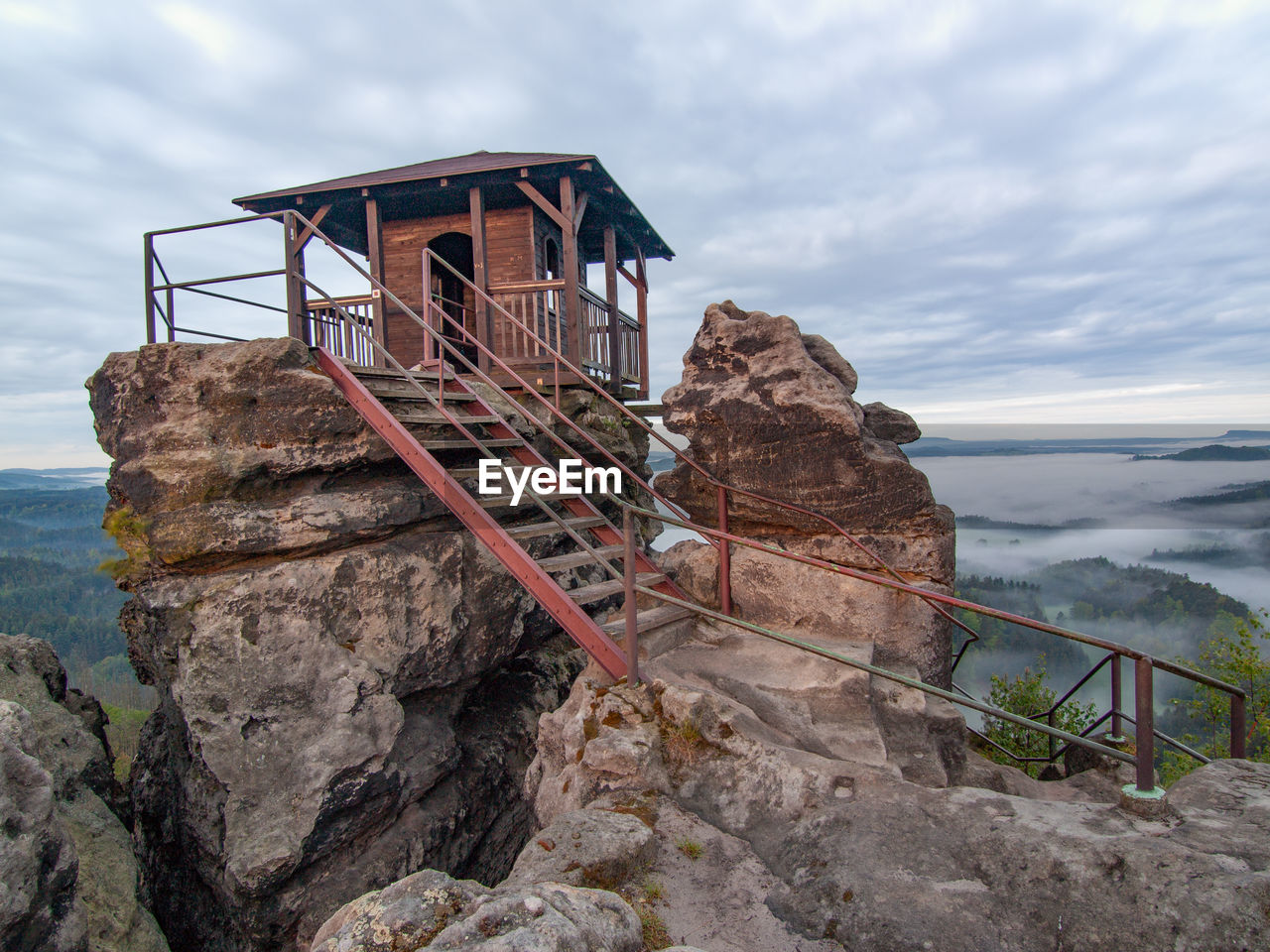 Tourist shelter or hut on rock by misty valley against sky