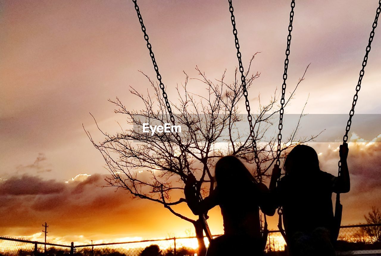 Silhouette children on swings against sky during sunset