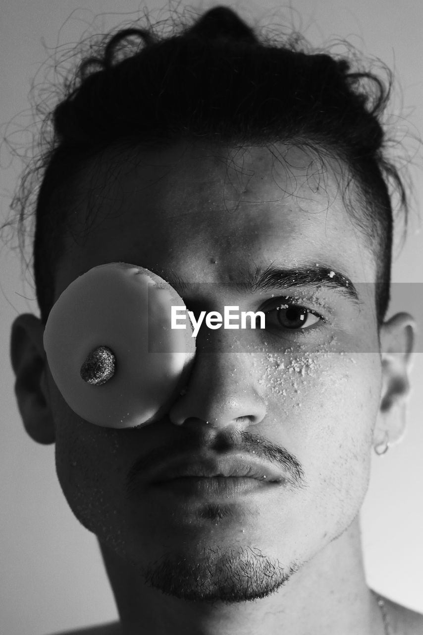 Close-up portrait of young man with food covering eye against wall