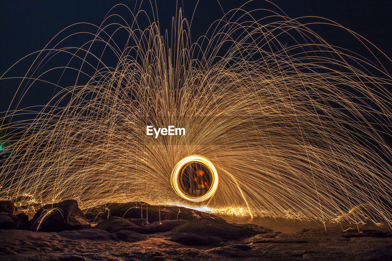 Person spinning wire wool at beach against sky