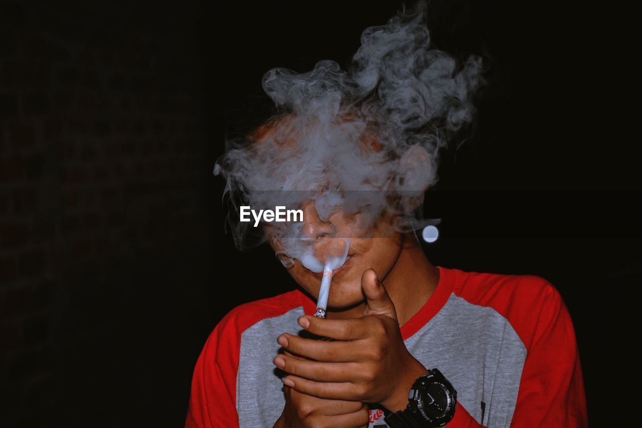 Portrait of man smoking against black background