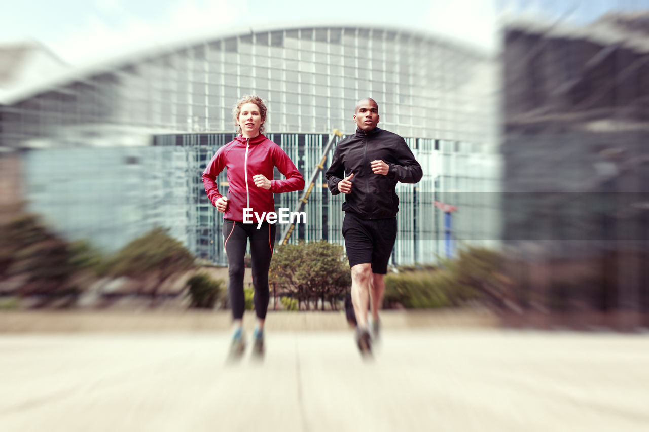 Full length of man jogging with woman against building