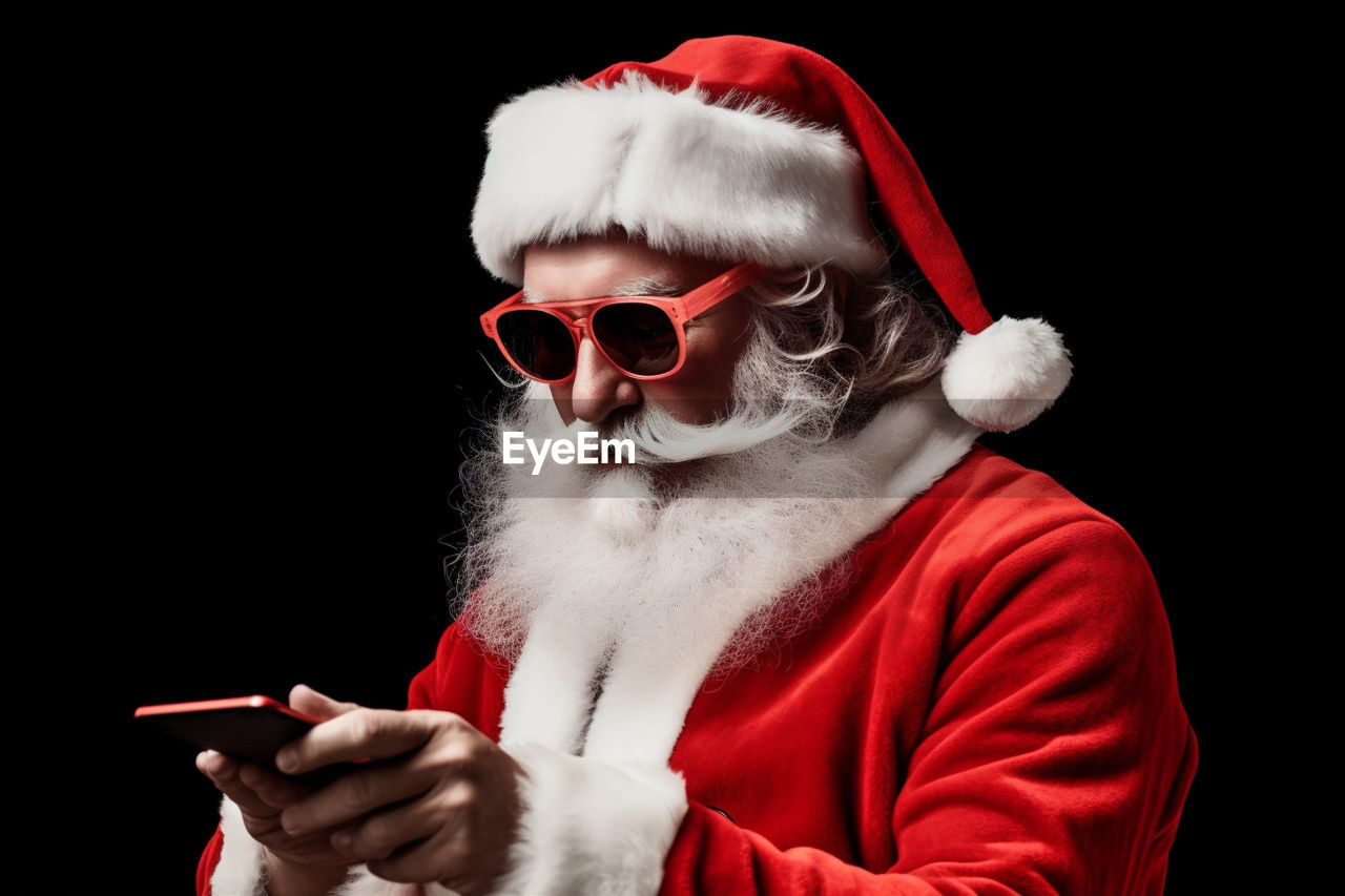 red, glasses, one person, black background, santa claus, sunglasses, studio shot, communication, facial hair, beard, fashion, adult, holding, celebration, hat, santa hat, men, portrait, christmas, person, costume, clothing, wireless technology, activity, indoors, holiday, human face, technology, dressing up, eyeglasses, human hair