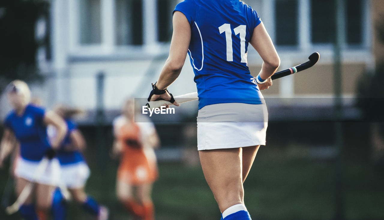 Midsection of hockey player holding bat while walking in stadium