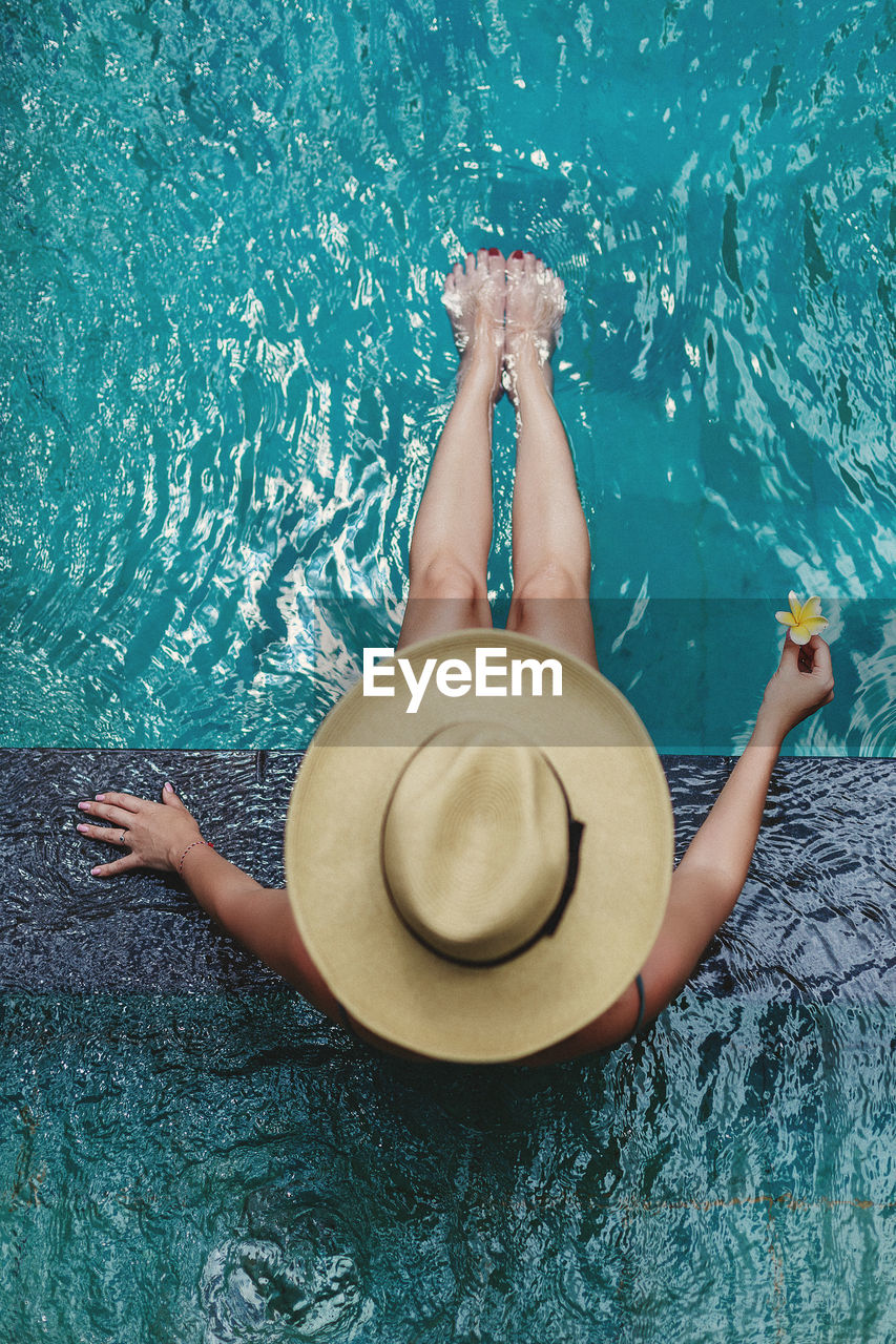 HIGH ANGLE VIEW OF WOMAN LYING ON SWIMMING POOL