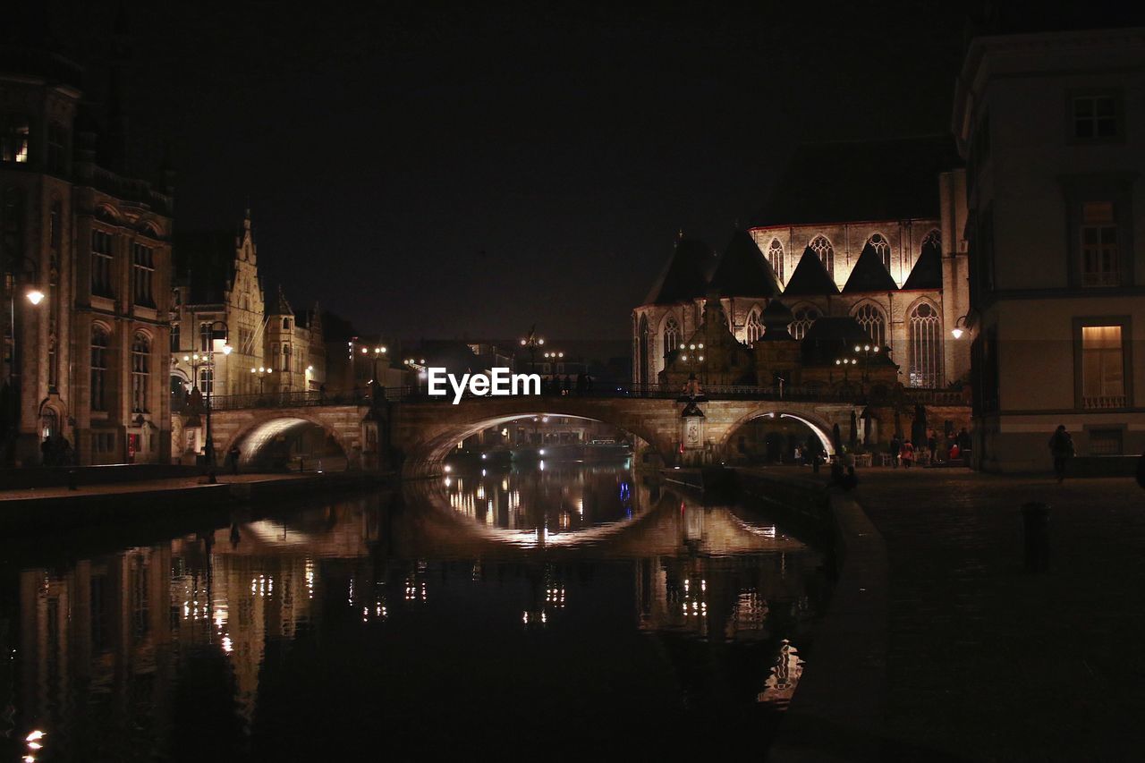 Illuminated bridge over river by buildings in city at night