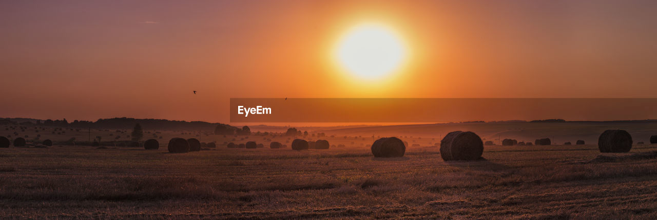 Hay bales on field against sky during sunset