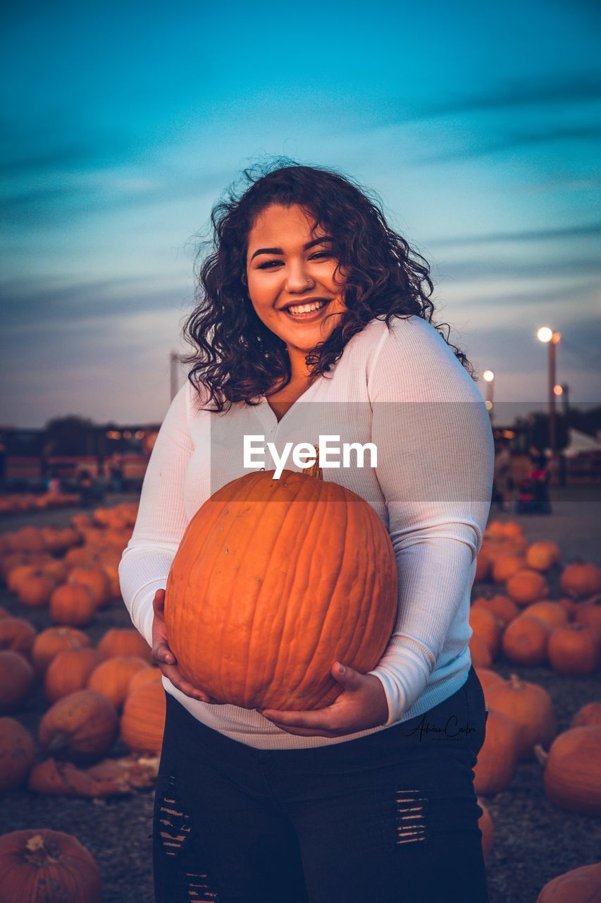 Portrait of smiling young woman holding pumpkin during sunset