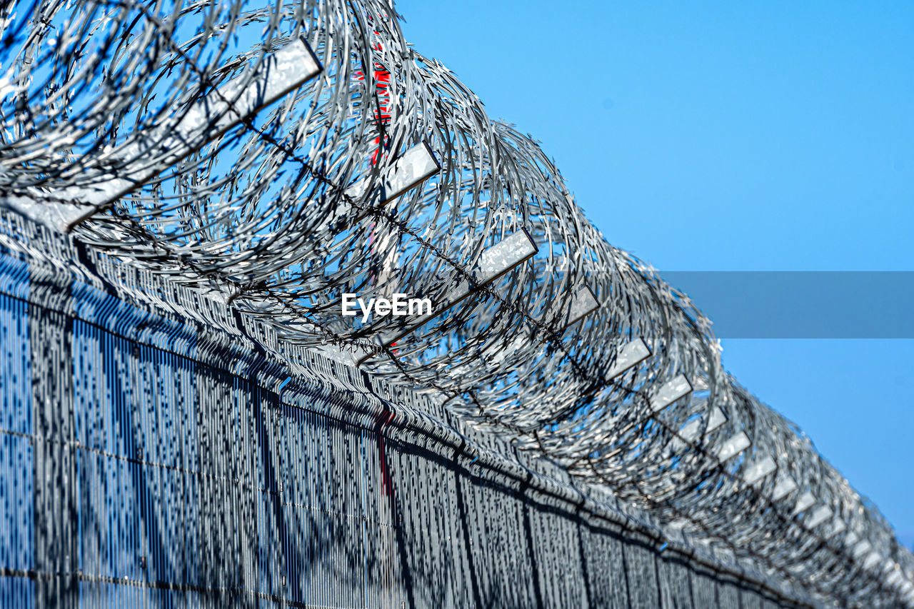 Fence with barbed wire against blue sky with clouds, security concept