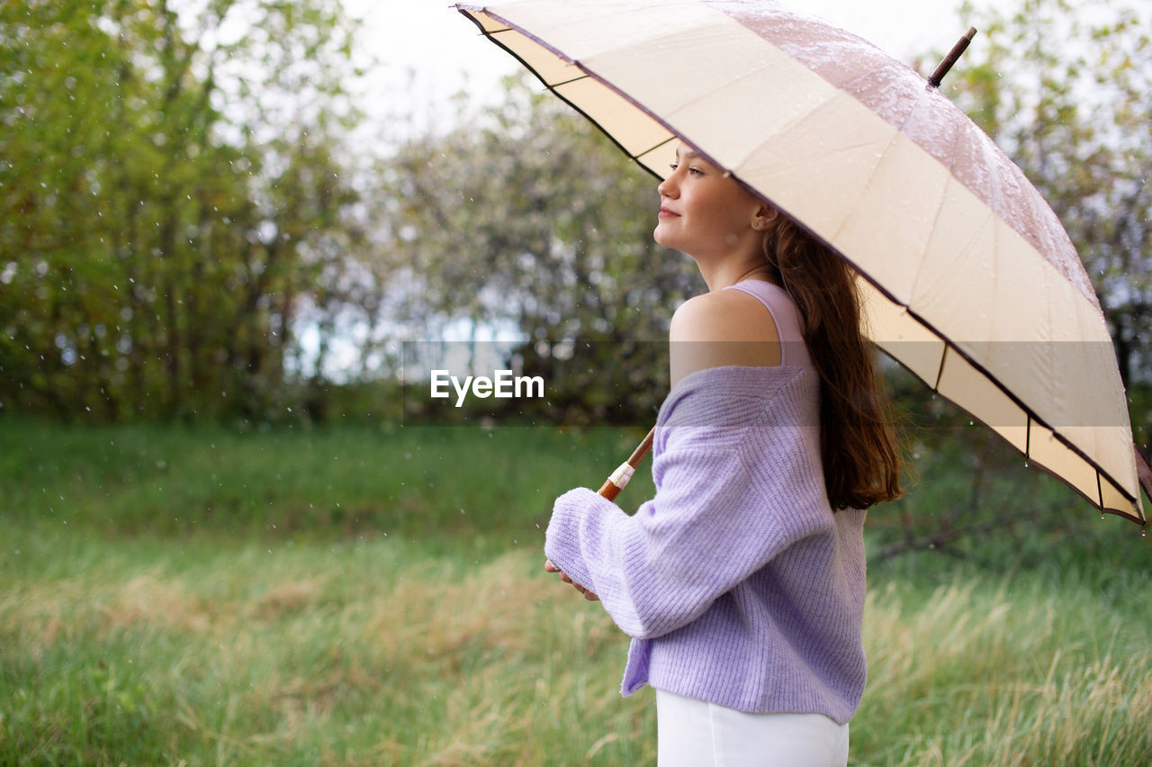 A girl in a sweater is standing under an umbrella. it's raining person