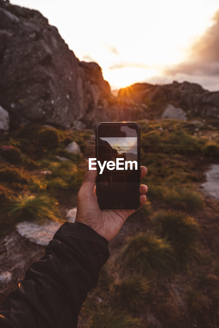 Hand holding smartphone with image of scene backlit by sunset