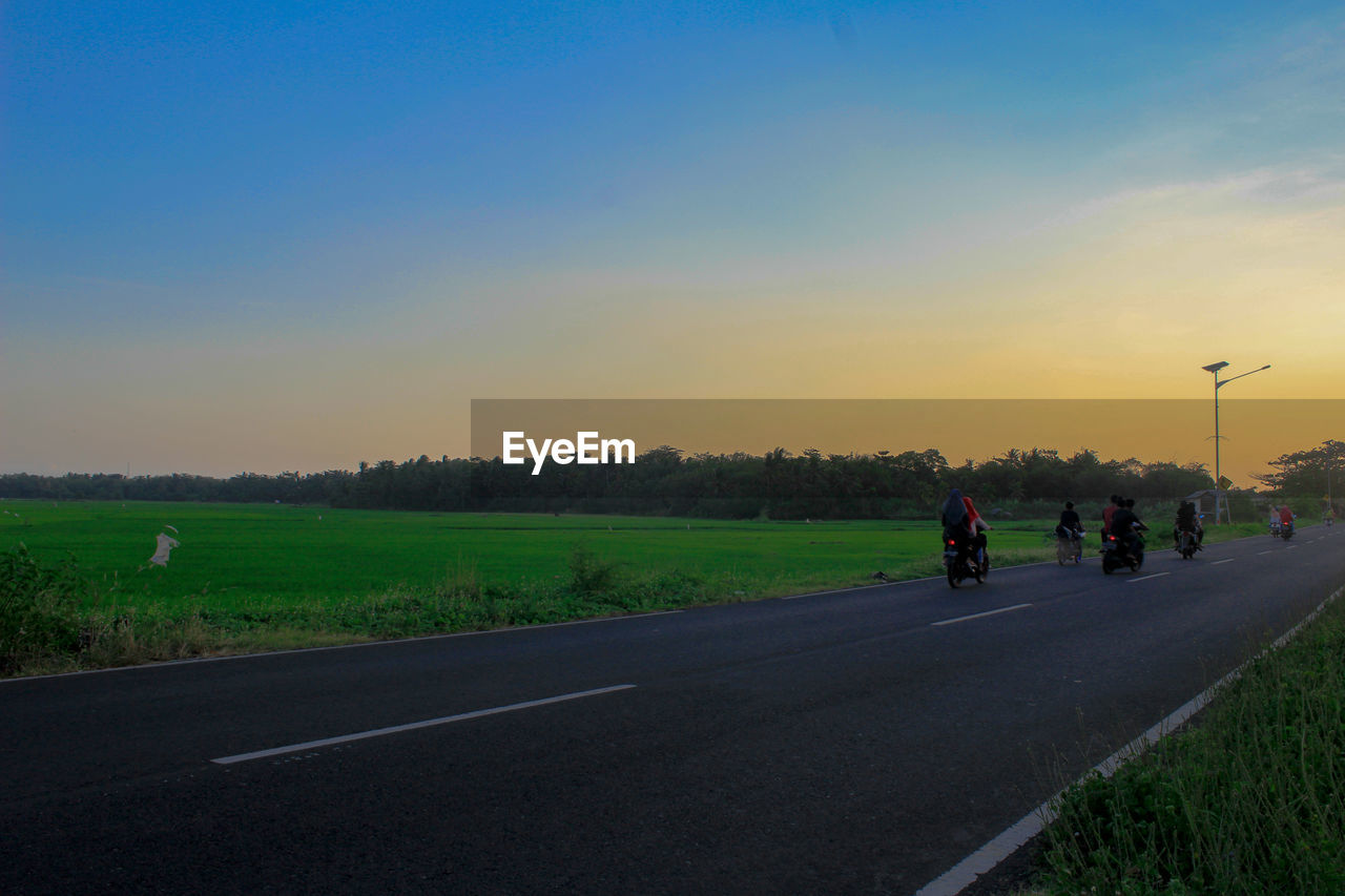 People riding motorcycle on road against sky during sunset