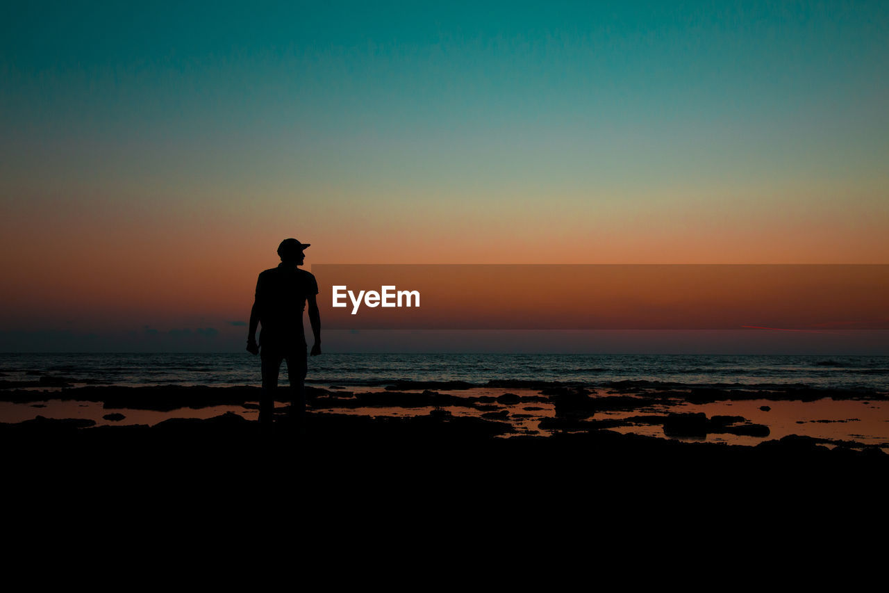 Silhouette man standing on beach against sky during sunset