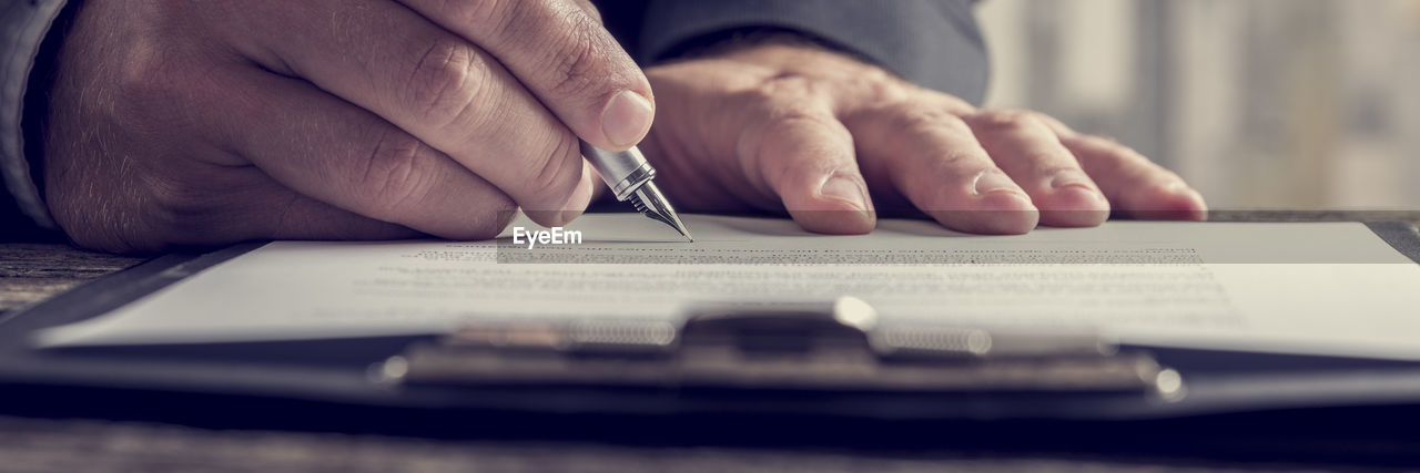 MIDSECTION OF MAN HOLDING PAPER WITH PEN