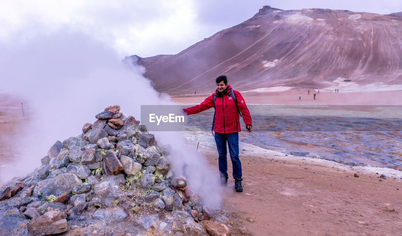 Smiling mature man standing by steam at geyser