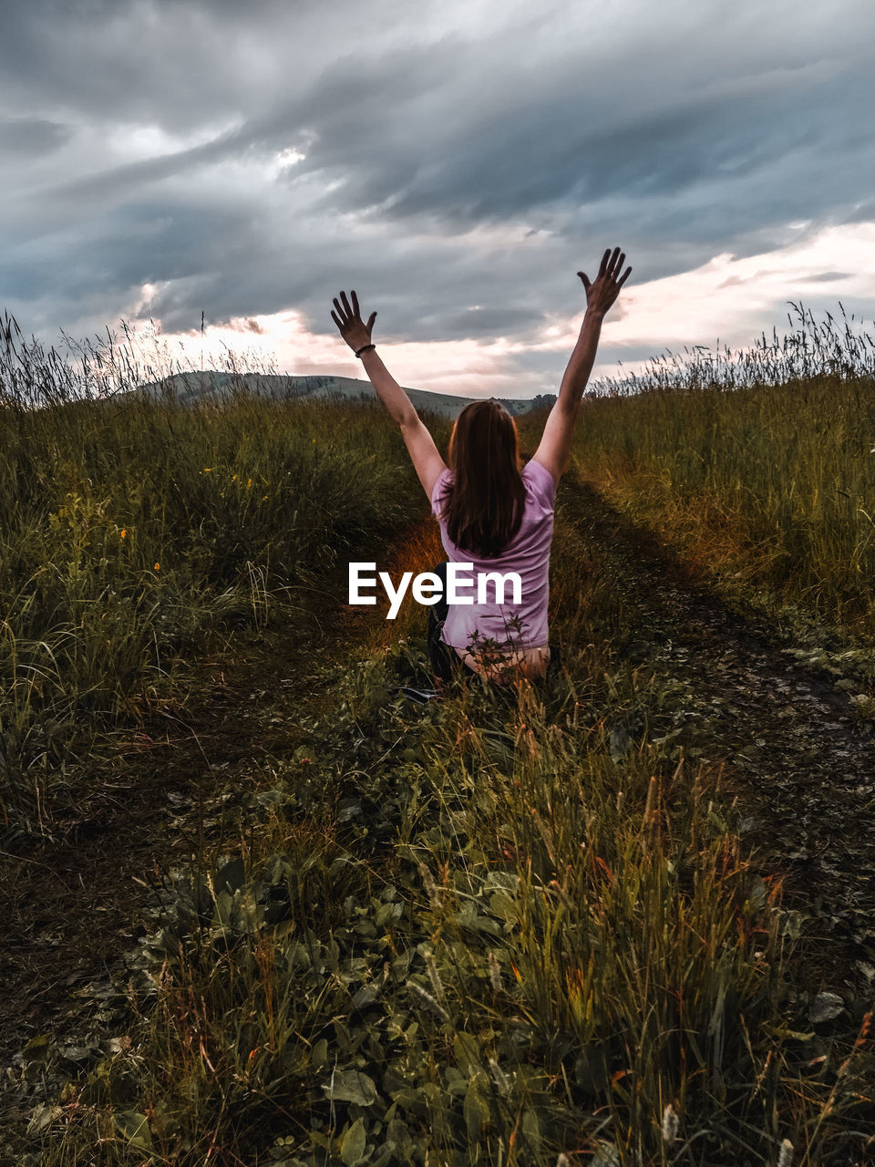 Rear view of woman with arms raised sitting on land