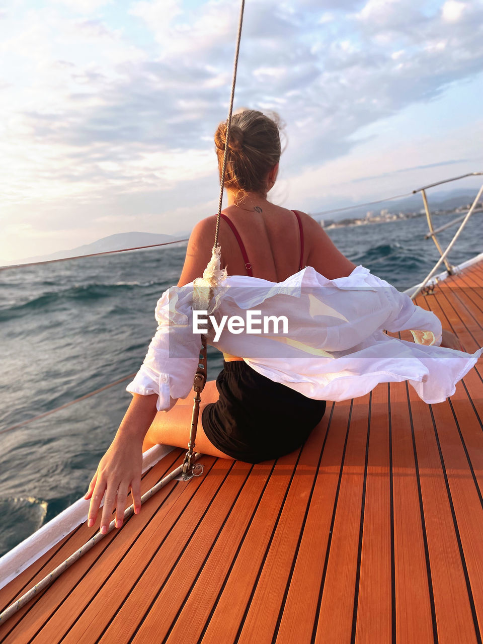 Rear view of woman sitting on pier over sea against sky