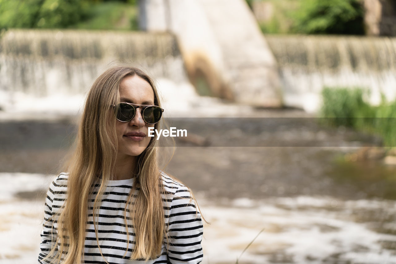 Portrait of a woman in a striped top and sunglasses in front of the dam by the river