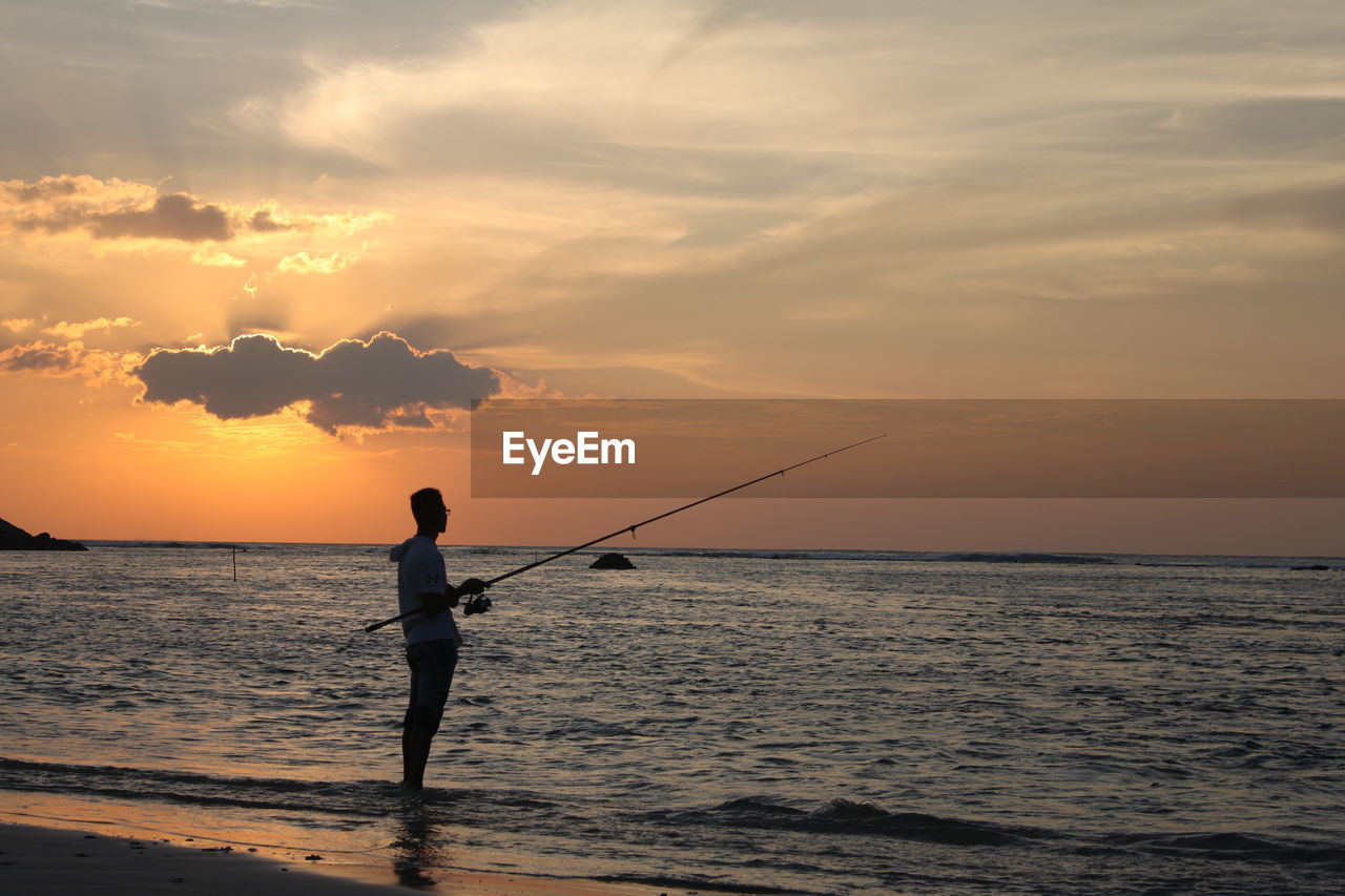 SILHOUETTE MAN FISHING IN SEA AGAINST SKY