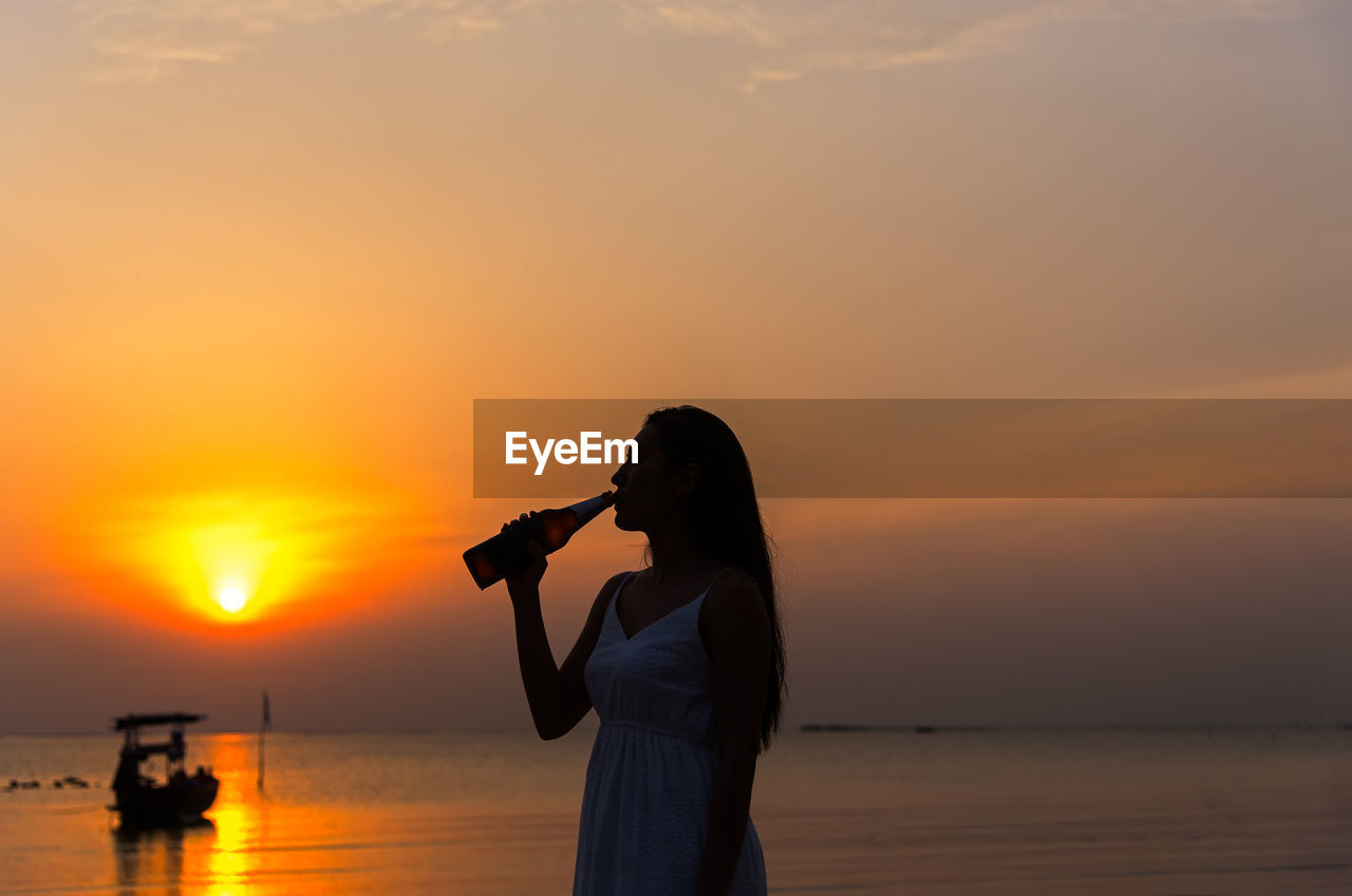 SILHOUETTE WOMAN PHOTOGRAPHING SEA AGAINST ORANGE SKY