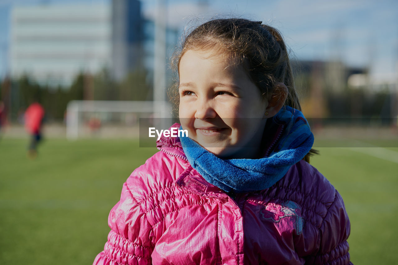 Smiling little girl wearing a pink coat in a football stadium