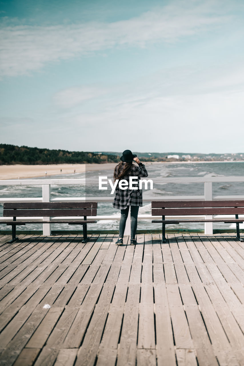 rear view of woman sitting on pier at sea