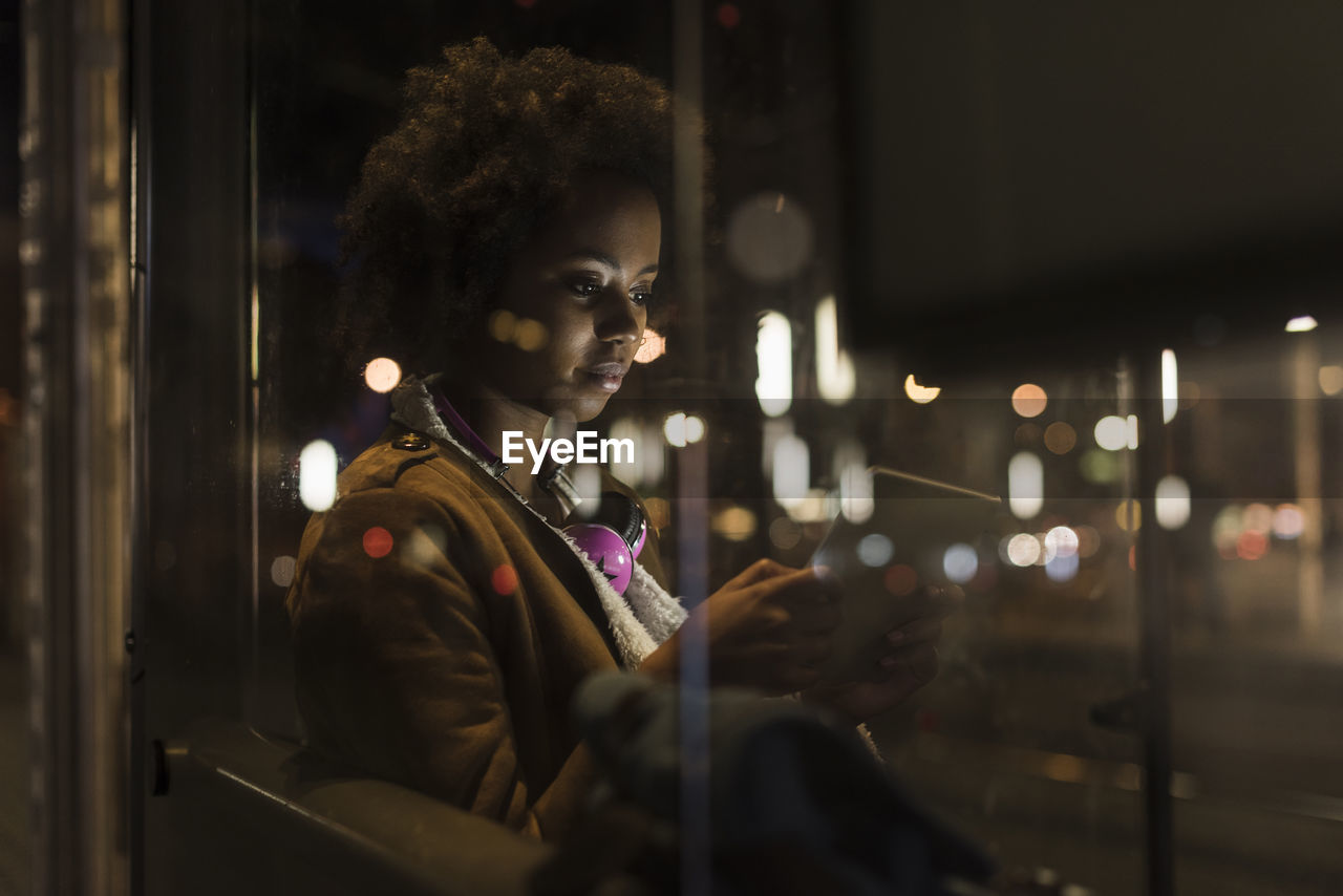 Young woman with tablet waiting at the tram stop by night