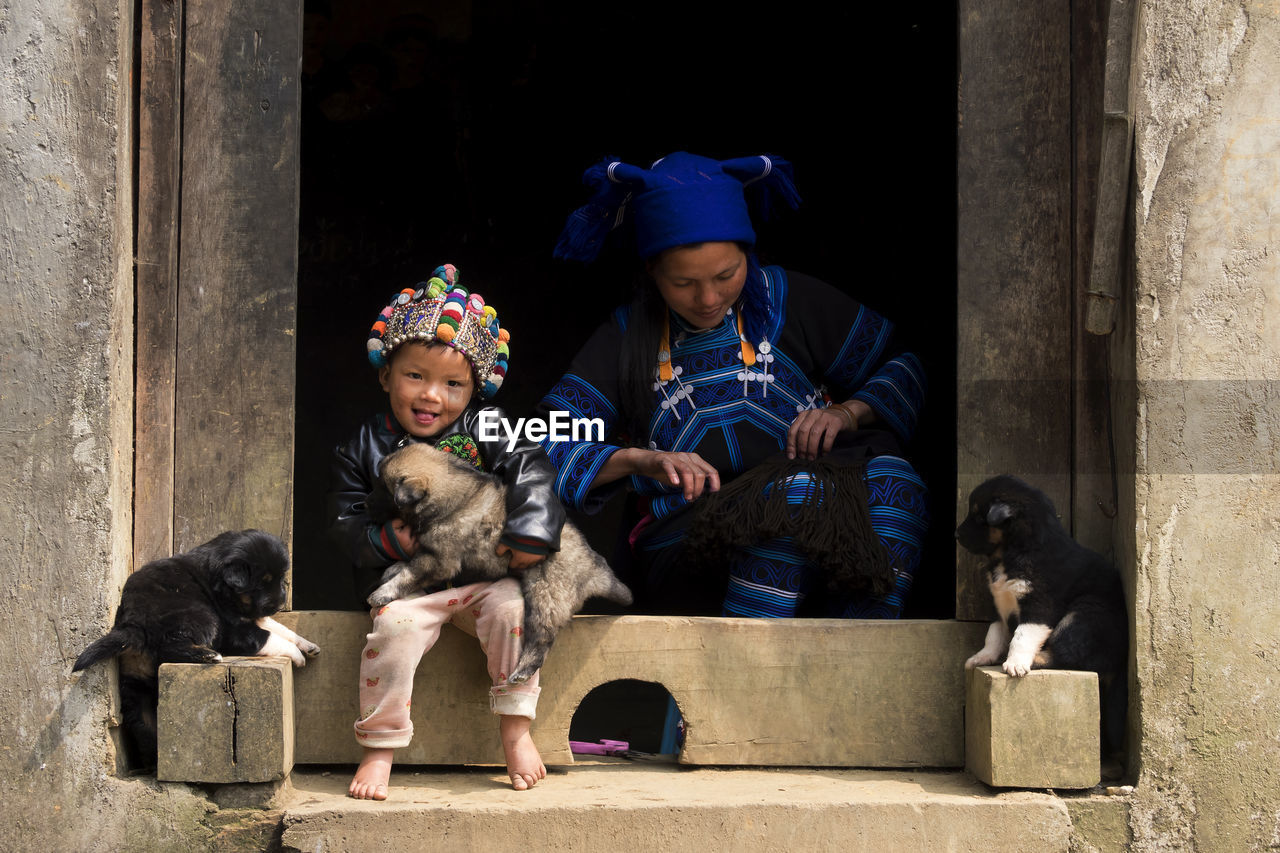 Portrait of smiling boy with dog by mother sitting at entrance