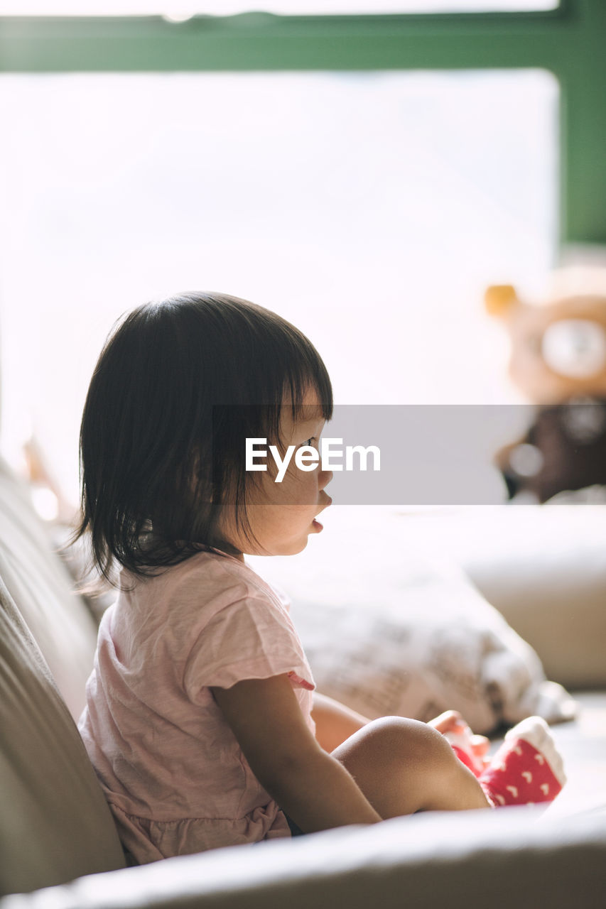 Side view of girl sitting on sofa in living room at home