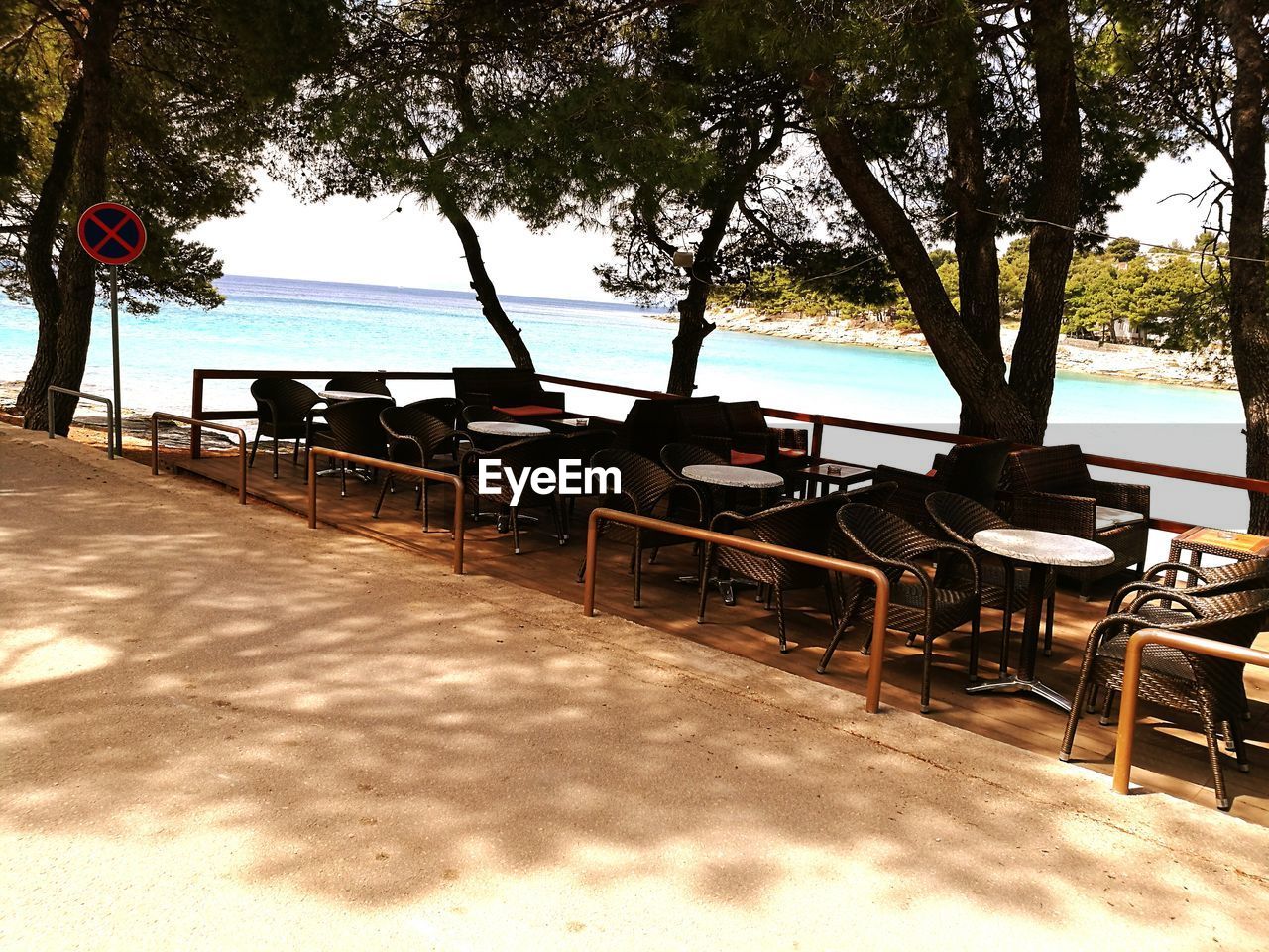 EMPTY CHAIRS AND TABLE BY BEACH AGAINST CLEAR SKY
