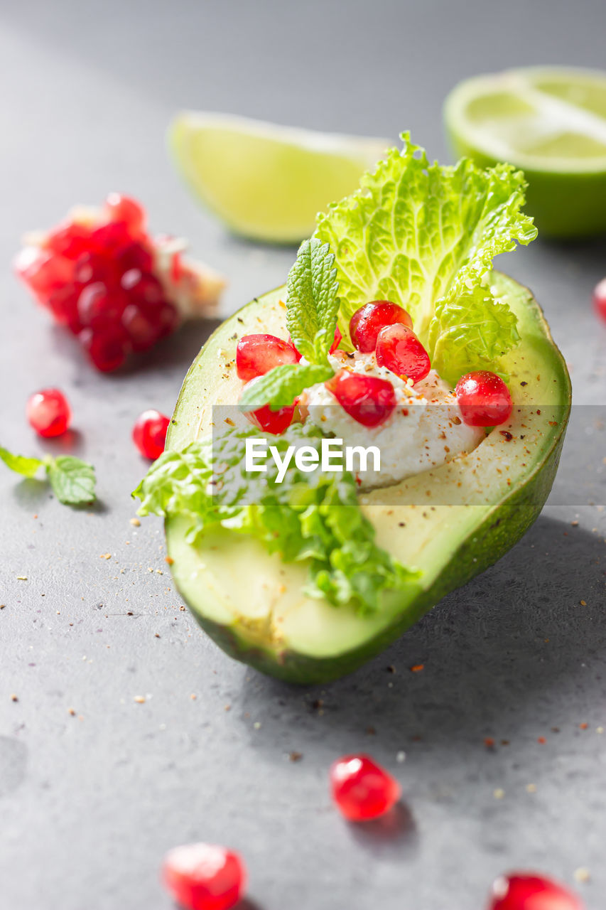 Halved avocado with cream cheese, pomegranate seeds, lettuce, mint and lime.