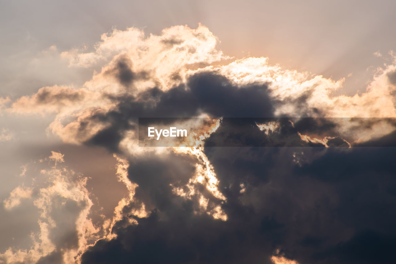 LOW ANGLE VIEW OF SUN STREAMING THROUGH CLOUDS DURING SUNSET