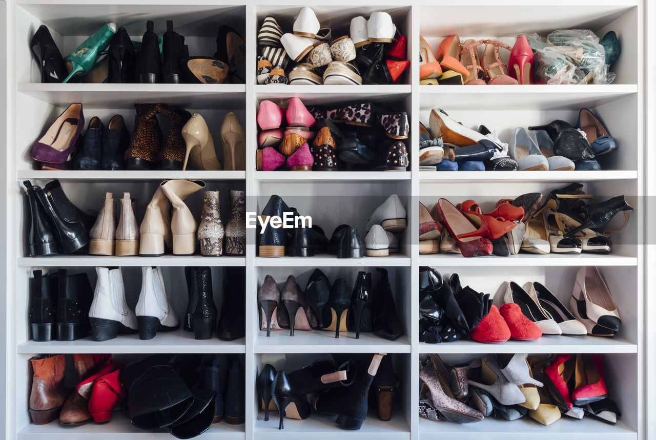 Modern white closet and square shelves with female colorful expensive high heels shoes and sneakers