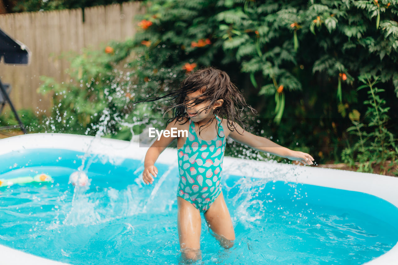 Diverse mixed race toddler girl at home having fun in kiddie pool in backyard being very happy