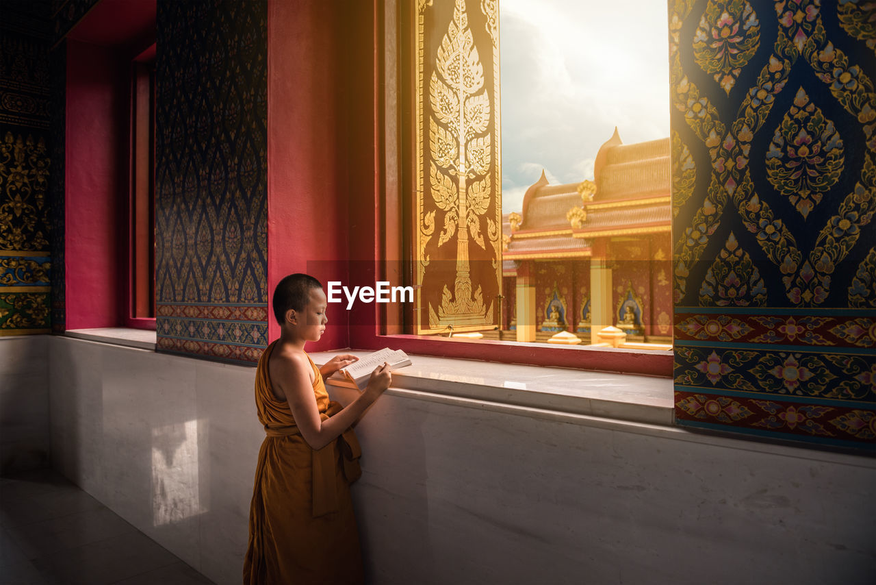 Monk reading book at window in temple