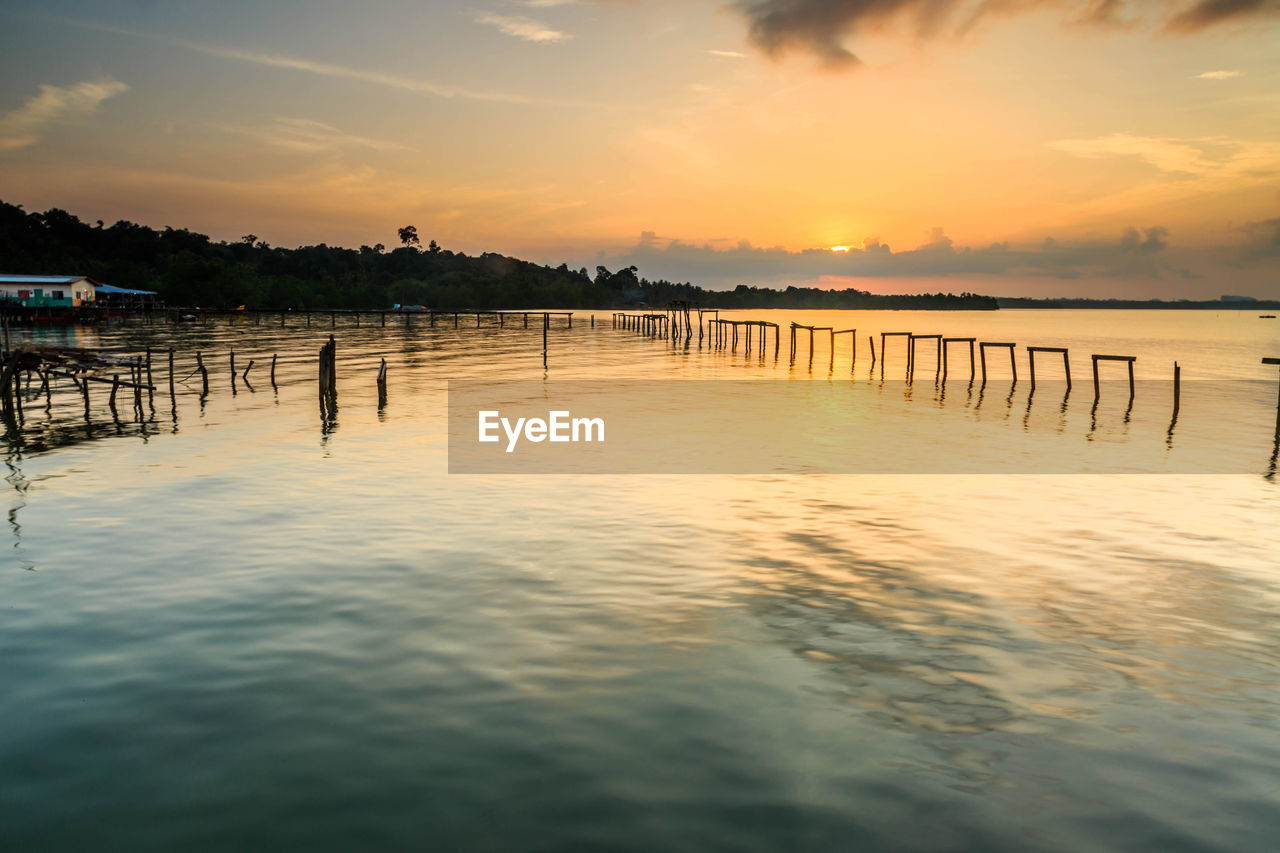 WOODEN POSTS IN SEA AGAINST SUNSET SKY