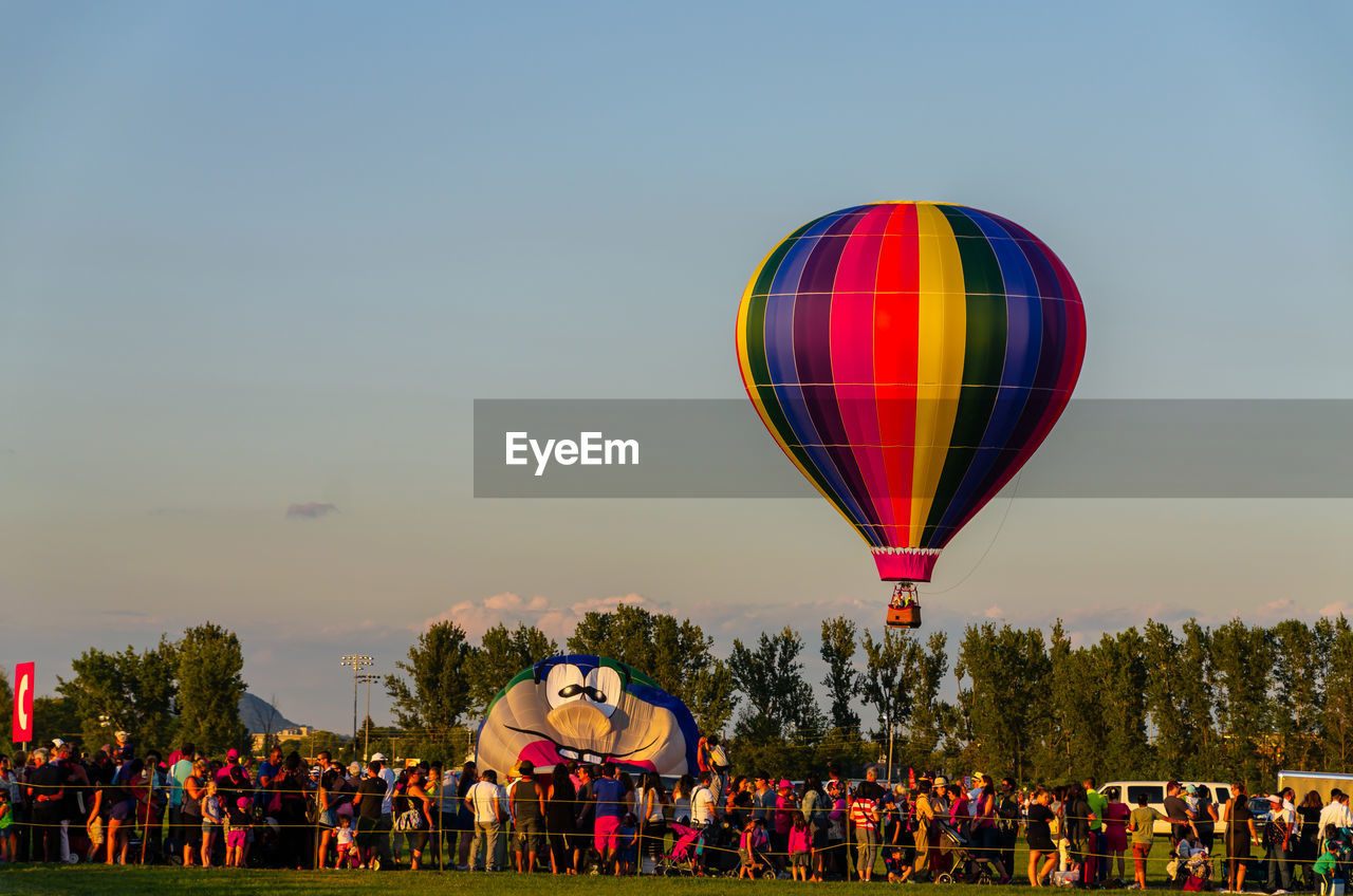 Group of people at hot air balloon festival against sky during sunset