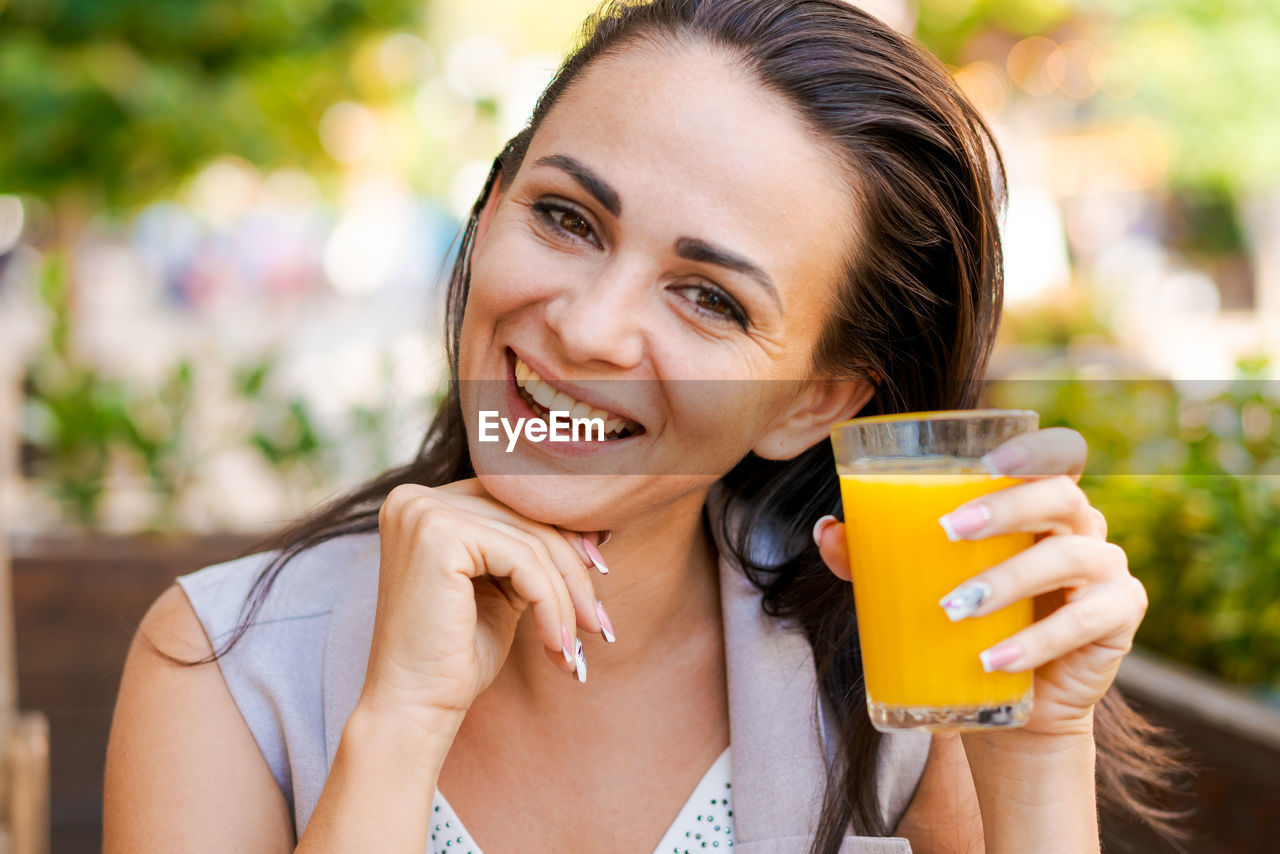 Happy business woman in street cafe drinks natural juice and smiles on sunny day.