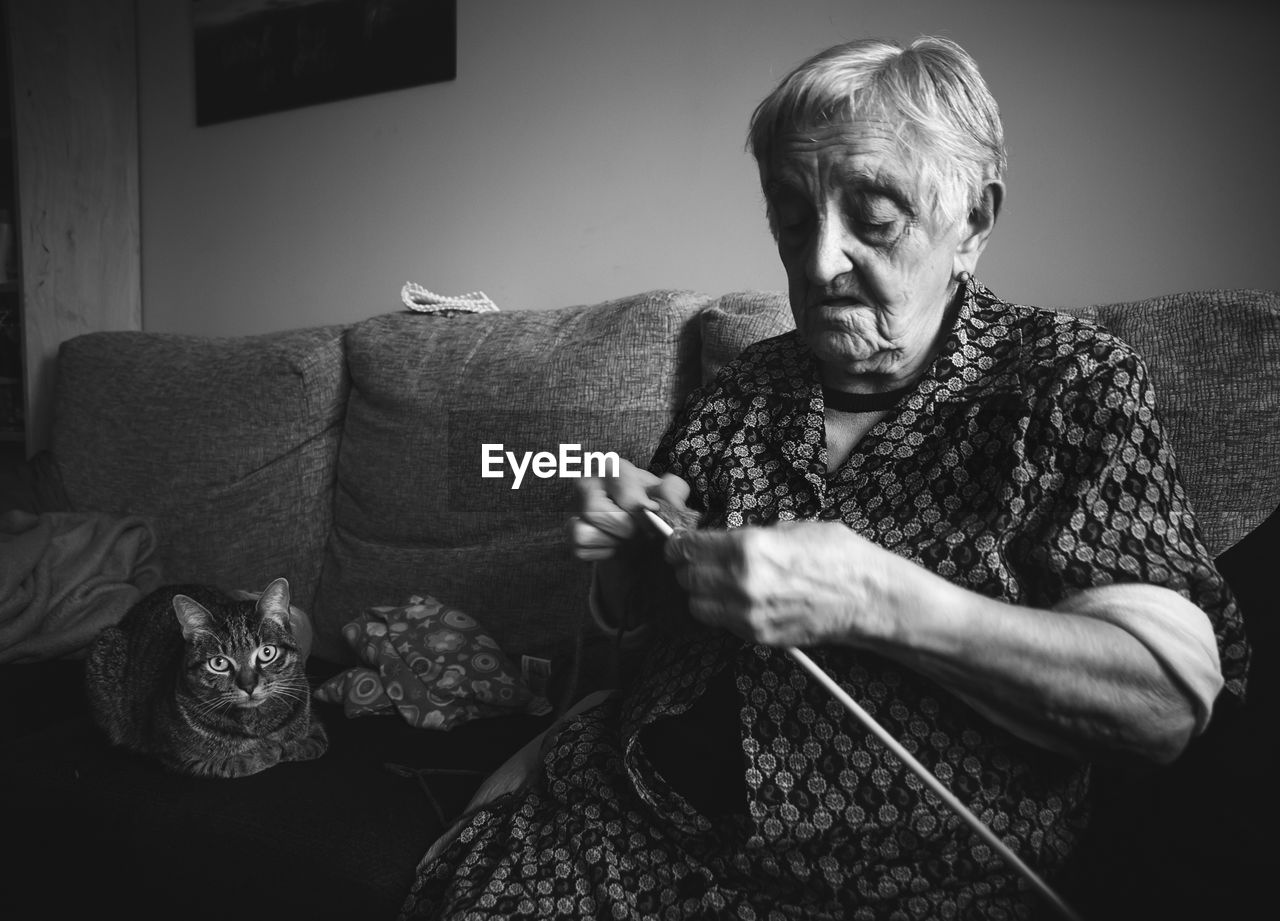 Senior woman knitting wool while sitting with cat on sofa at home